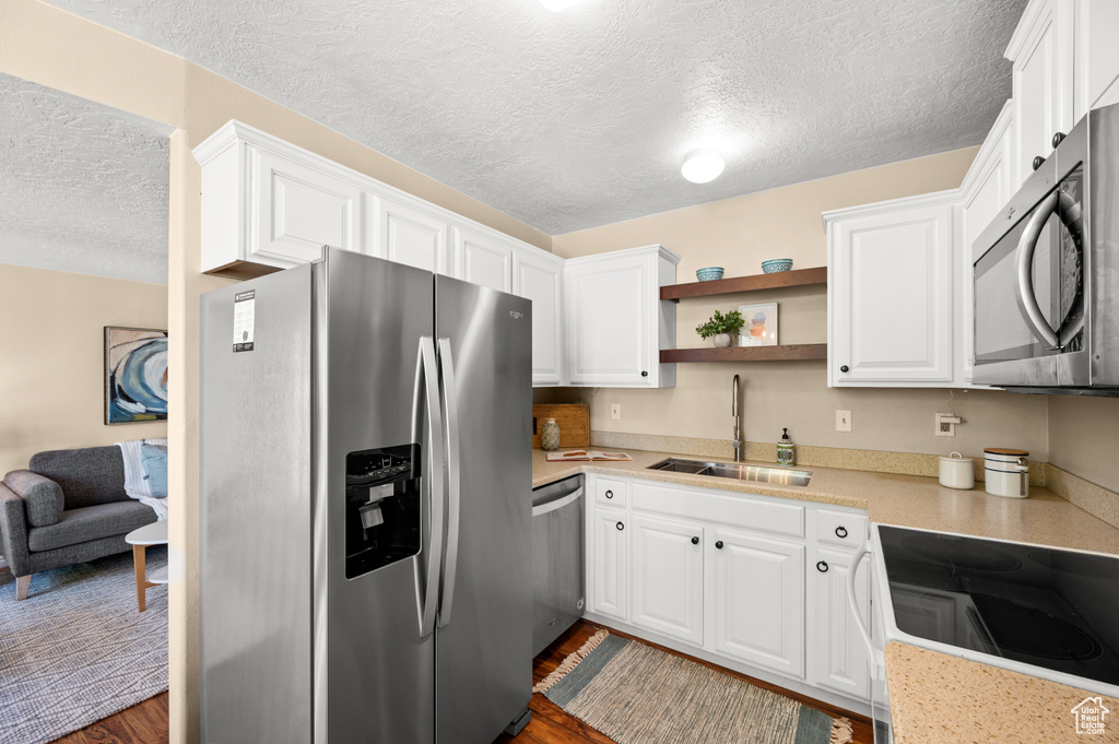 Kitchen with a textured ceiling, appliances with stainless steel finishes, a sink, light countertops, and white cabinetry