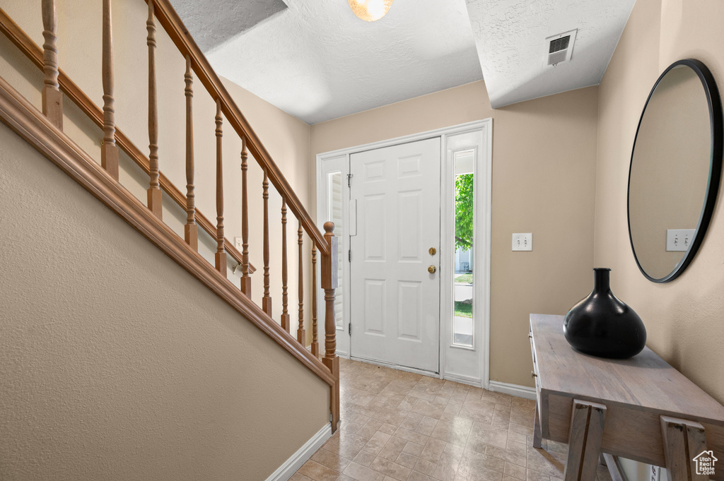 Foyer entrance featuring visible vents, a textured ceiling, baseboards, and stairway
