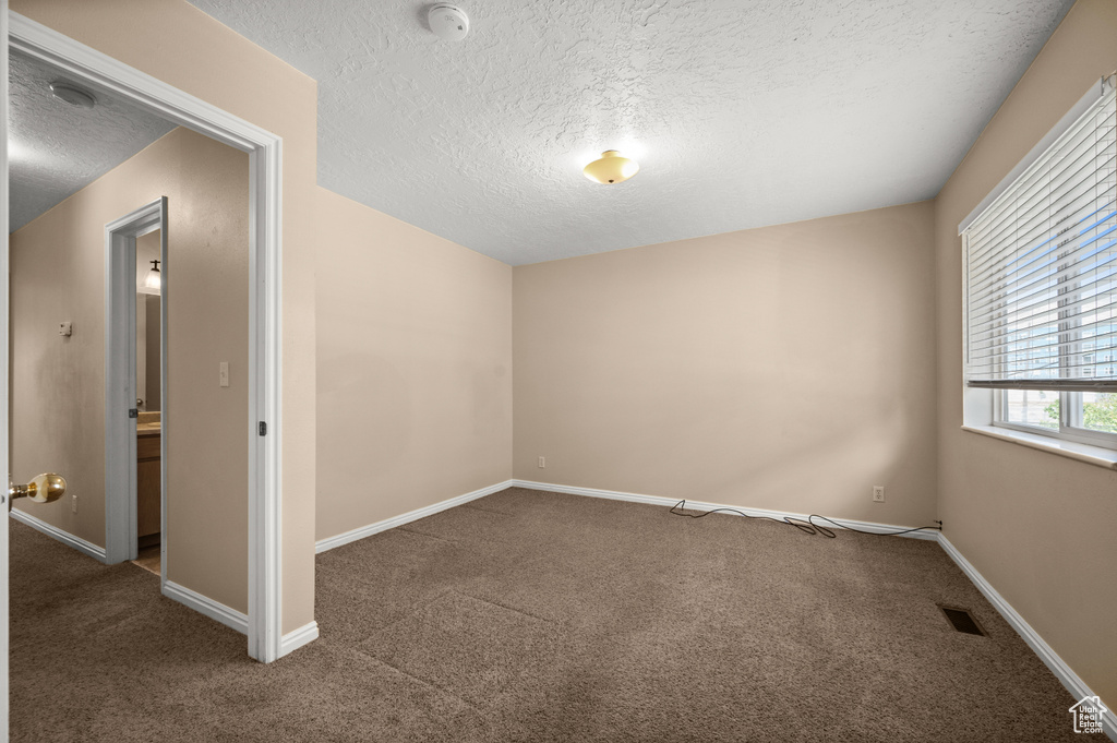 Carpeted spare room with visible vents, a textured ceiling, and baseboards