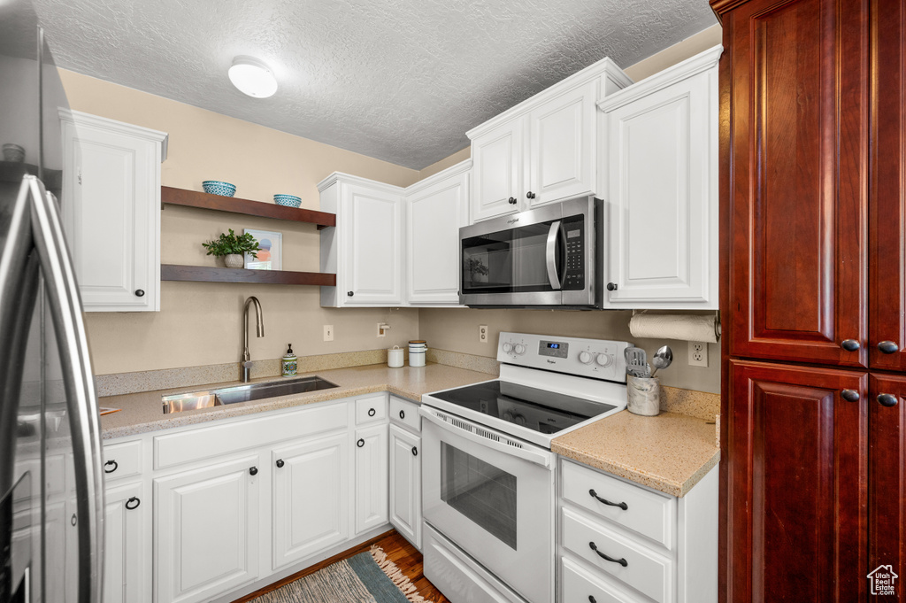 Kitchen featuring open shelves, a sink, light countertops, a textured ceiling, and stainless steel appliances
