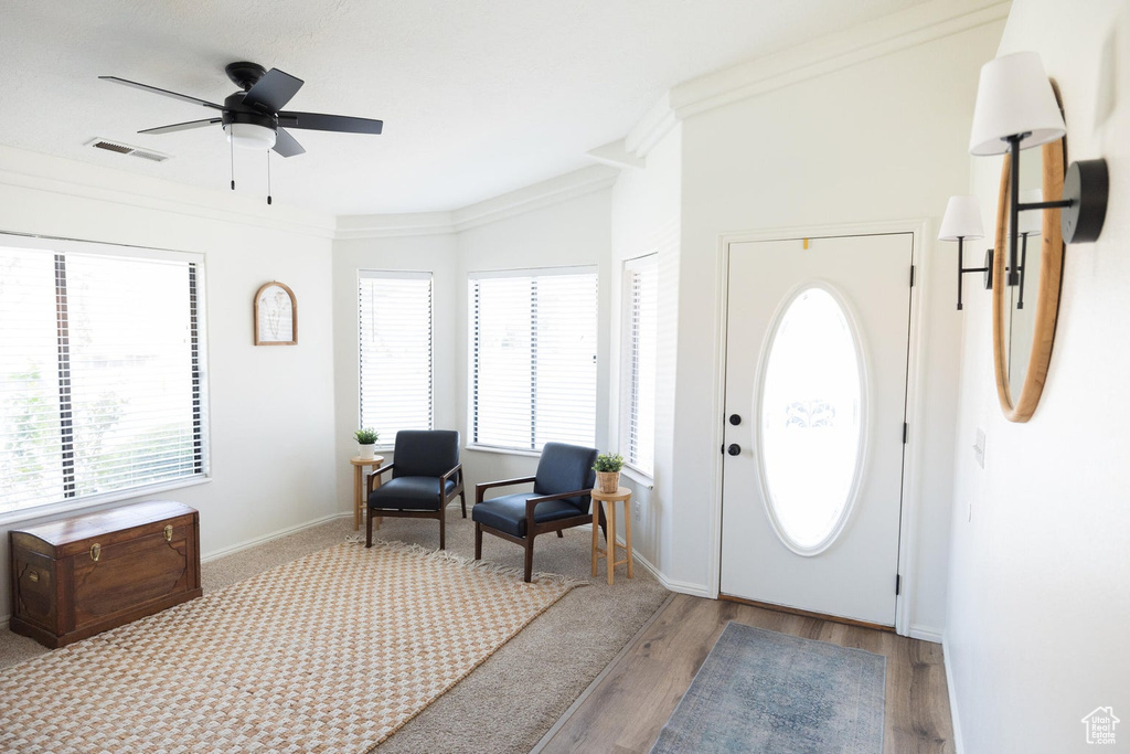 Entryway with a ceiling fan, visible vents, crown molding, wood finished floors, and baseboards
