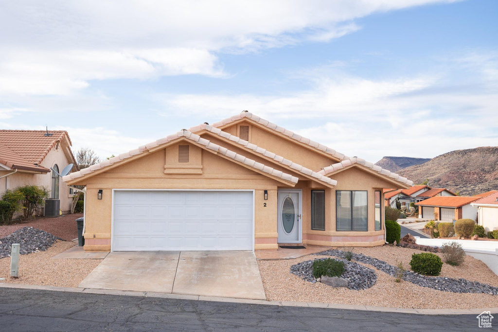 Ranch-style home featuring an attached garage, stucco siding, a mountain view, a tiled roof, and driveway