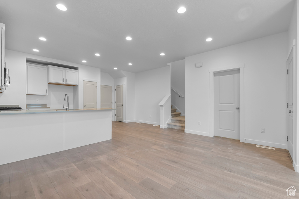 Unfurnished living room featuring stairs, recessed lighting, a sink, and light wood finished floors