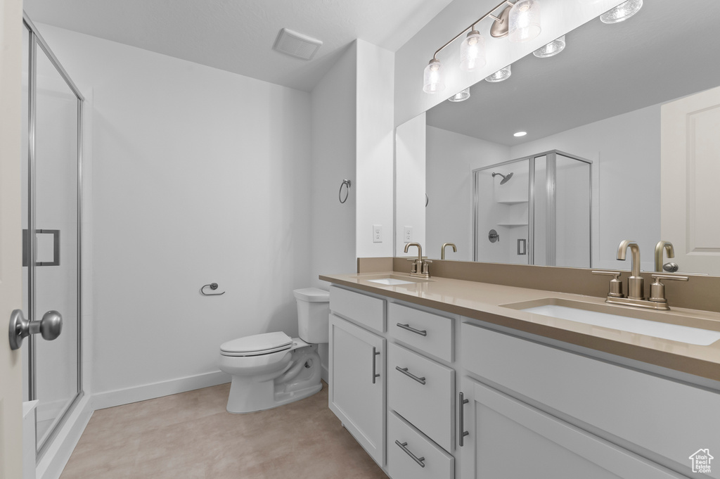 Bathroom featuring a sink, a shower stall, toilet, and double vanity