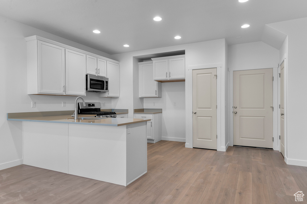 Kitchen featuring baseboards, white cabinets, light wood finished floors, a peninsula, and stainless steel appliances