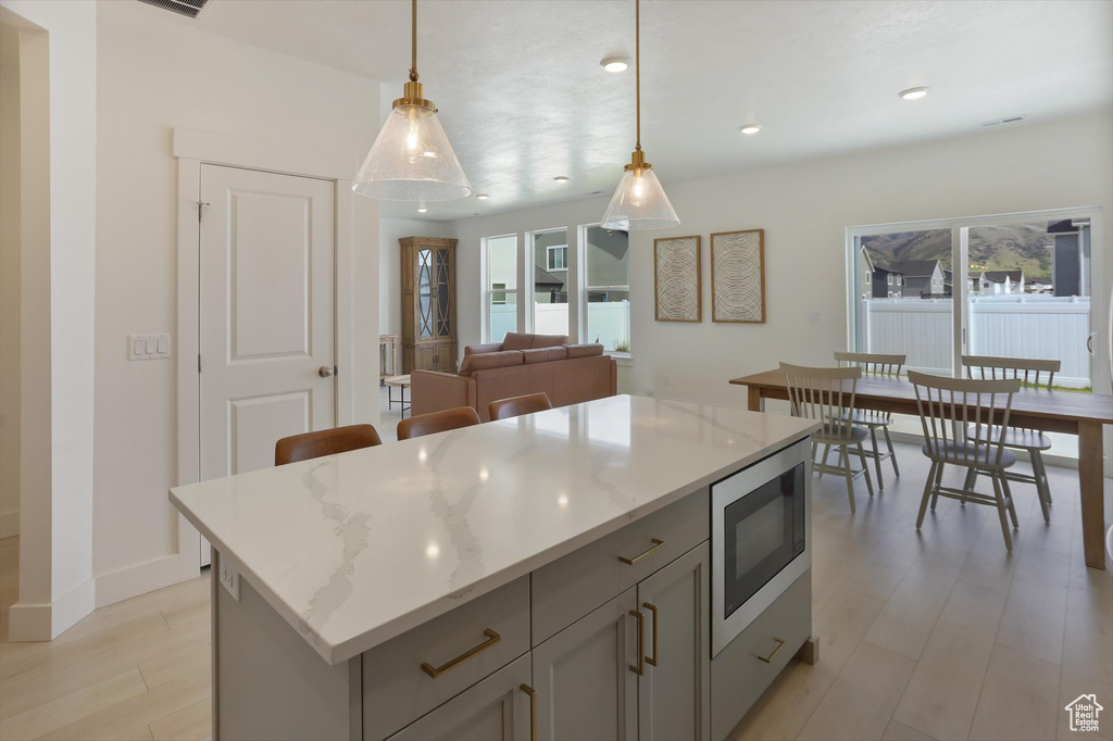 Kitchen featuring light wood-style flooring, recessed lighting, stainless steel microwave, a kitchen island, and pendant lighting