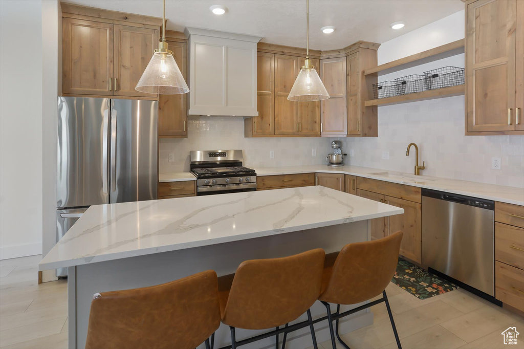 Kitchen featuring open shelves, appliances with stainless steel finishes, a sink, a kitchen breakfast bar, and decorative backsplash