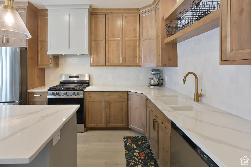 Kitchen with backsplash, appliances with stainless steel finishes, a sink, and light stone counters