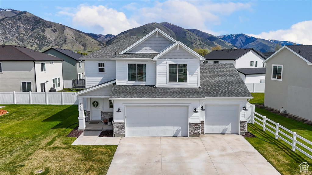 View of front of home featuring a front yard, stone siding, roof with shingles, a mountain view, and driveway