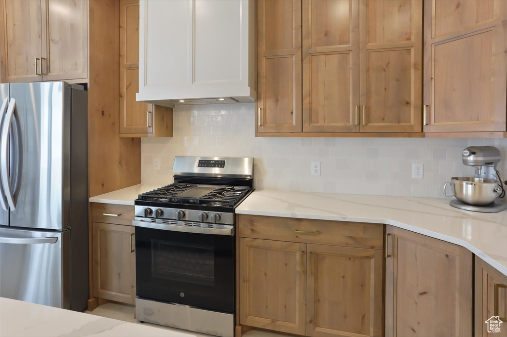 Kitchen featuring light stone counters, decorative backsplash, and stainless steel appliances