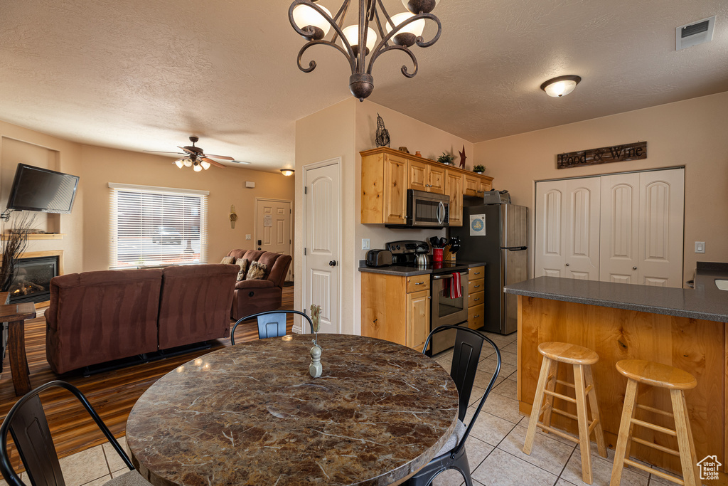 Dining area featuring light tile patterned floors, a textured ceiling, ceiling fan, a glass covered fireplace, and a chandelier
