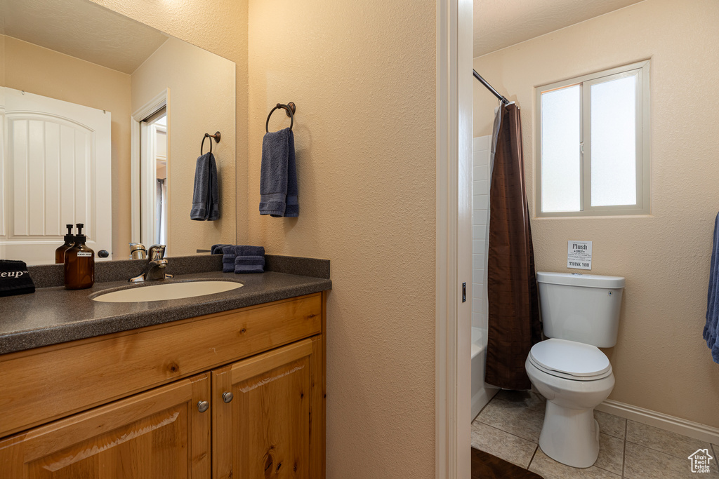 Full bathroom with toilet, tile patterned floors, vanity, shower / tub combo, and baseboards