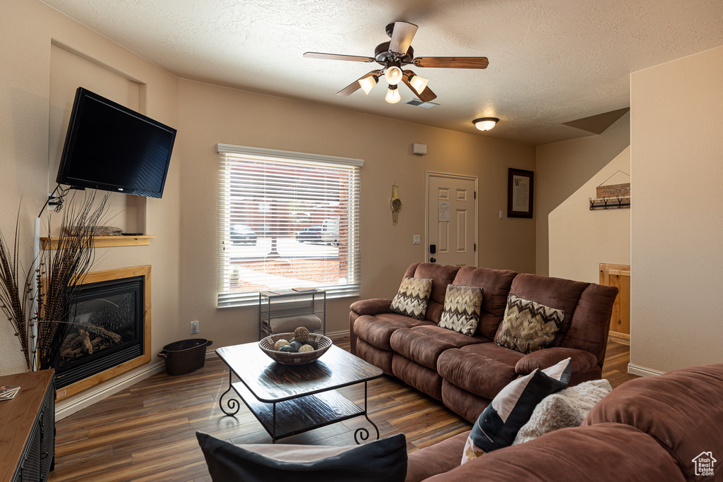 Living room featuring wood finished floors, a glass covered fireplace, ceiling fan, a textured ceiling, and baseboards