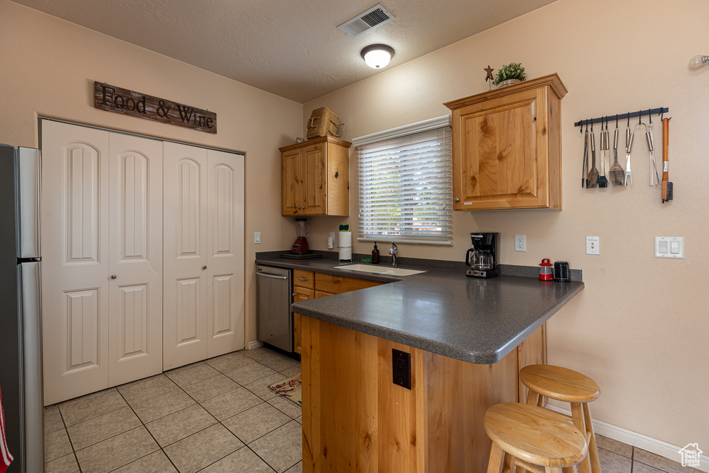 Kitchen featuring stainless steel appliances, a sink, dark countertops, light tile patterned floors, and a peninsula