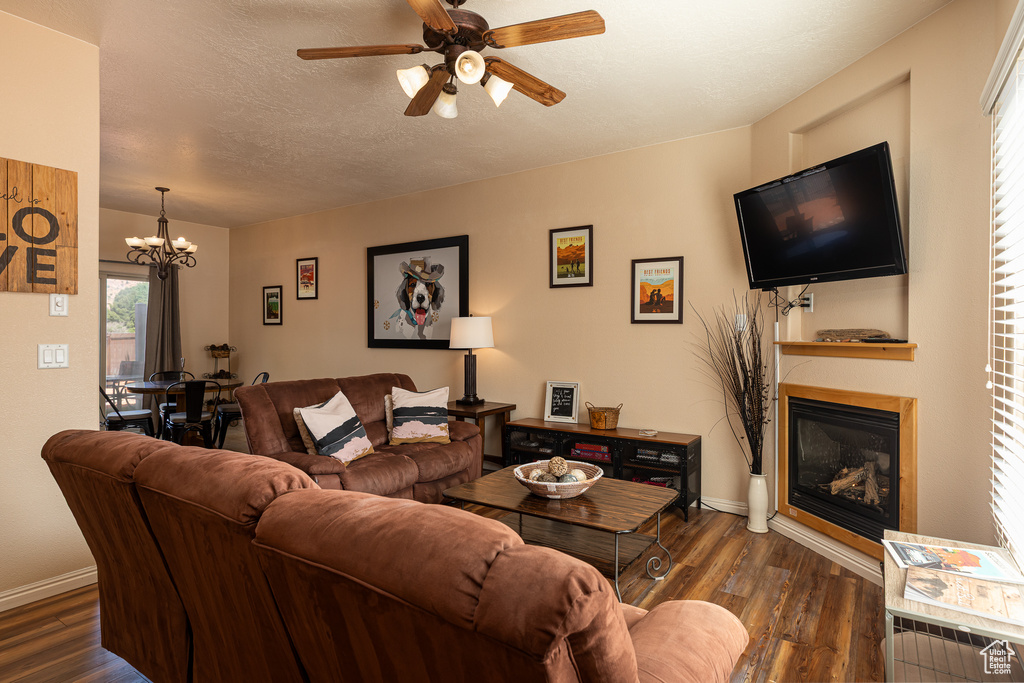 Living room with a glass covered fireplace, dark wood-style flooring, a chandelier, a ceiling fan, and baseboards