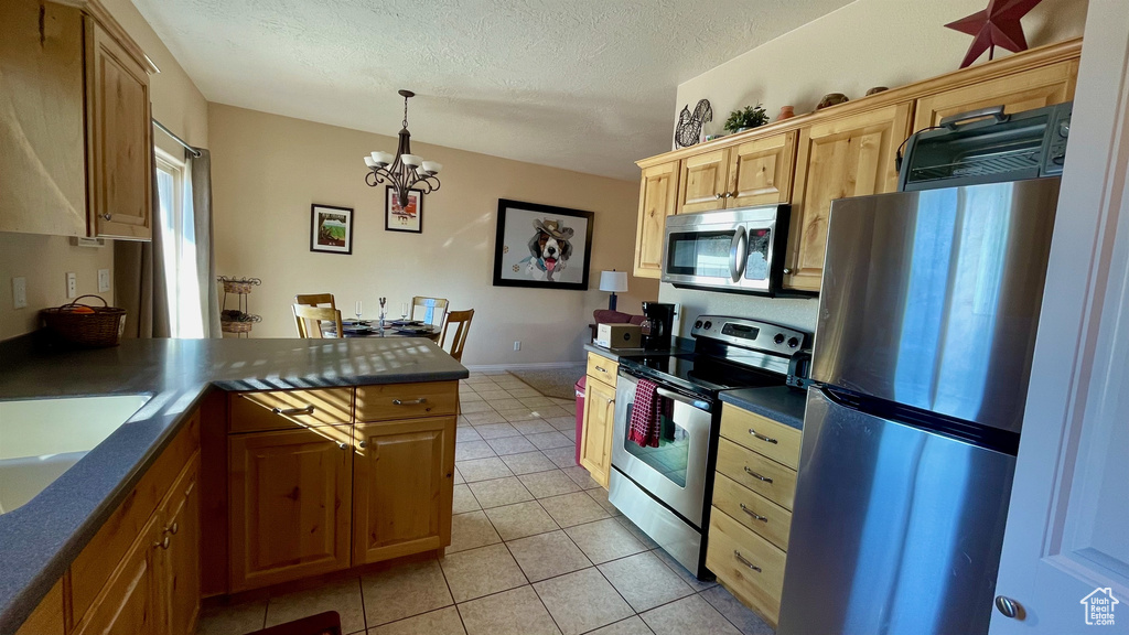 Kitchen featuring dark countertops, appliances with stainless steel finishes, a chandelier, a peninsula, and light tile patterned floors