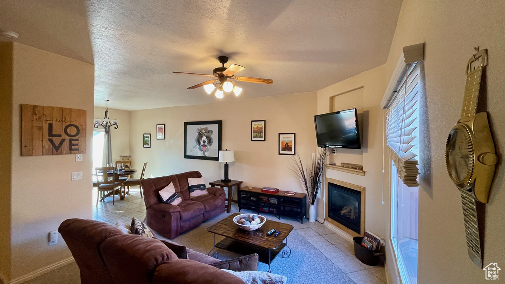Living area featuring a glass covered fireplace, ceiling fan with notable chandelier, and light tile patterned flooring
