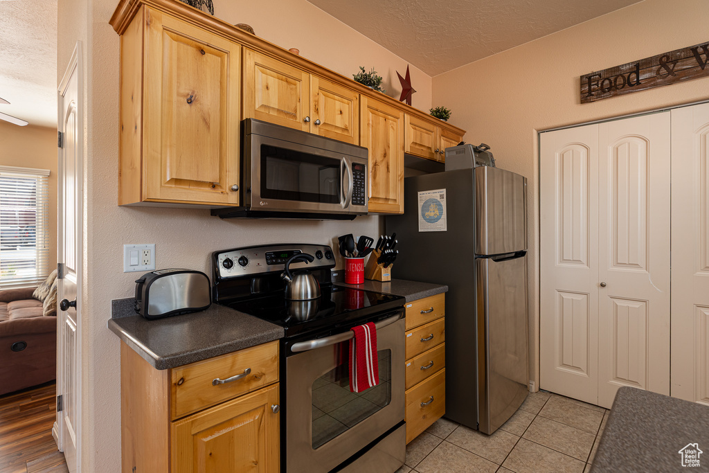 Kitchen with stainless steel appliances, a textured ceiling, dark countertops, and light tile patterned floors