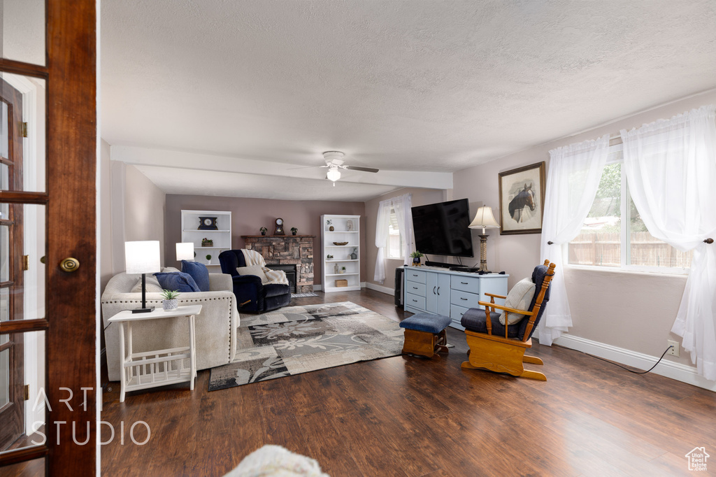 Living room featuring a ceiling fan, a textured ceiling, a fireplace, wood finished floors, and baseboards