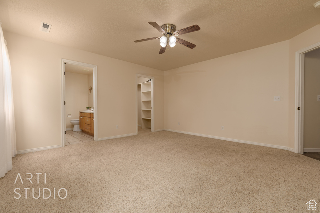 Unfurnished bedroom featuring a walk in closet, visible vents, light colored carpet, baseboards, and connected bathroom