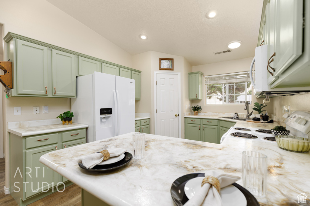 Kitchen with green cabinetry, a sink, white appliances, wood finished floors, and visible vents
