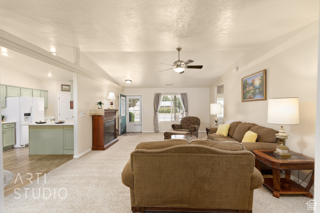 Living room featuring a glass covered fireplace, ceiling fan, light colored carpet, a textured ceiling, and vaulted ceiling