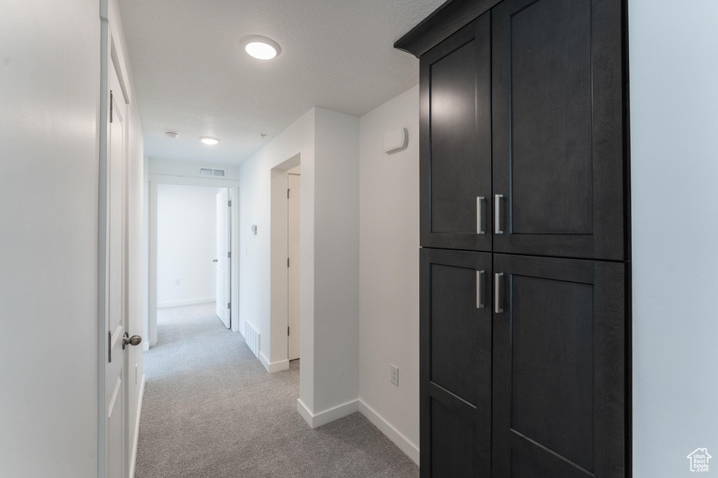 Hall with light colored carpet, baseboards, and visible vents