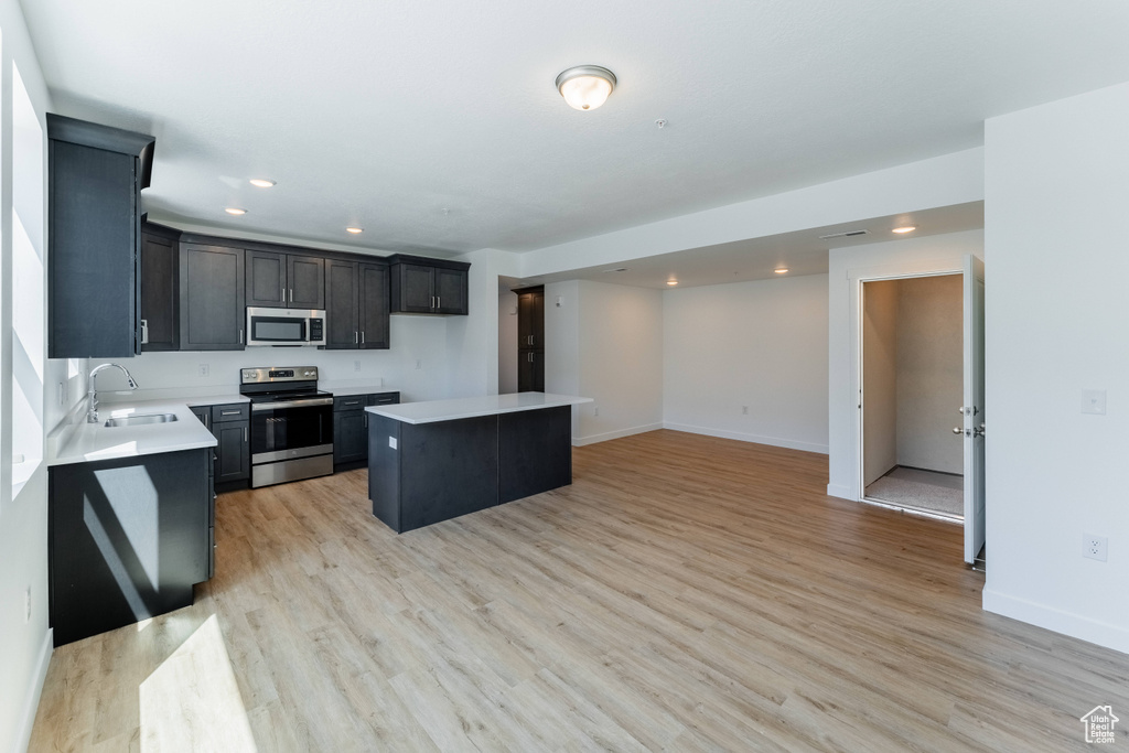 Kitchen featuring appliances with stainless steel finishes, a sink, light countertops, recessed lighting, and a kitchen island