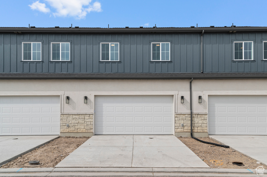Townhome / multi-family property featuring board and batten siding, an attached garage, and stone siding