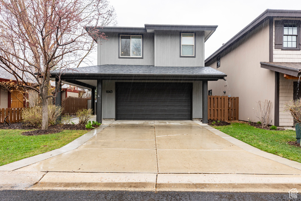 Traditional home with a garage, roof with shingles, fence, and concrete driveway