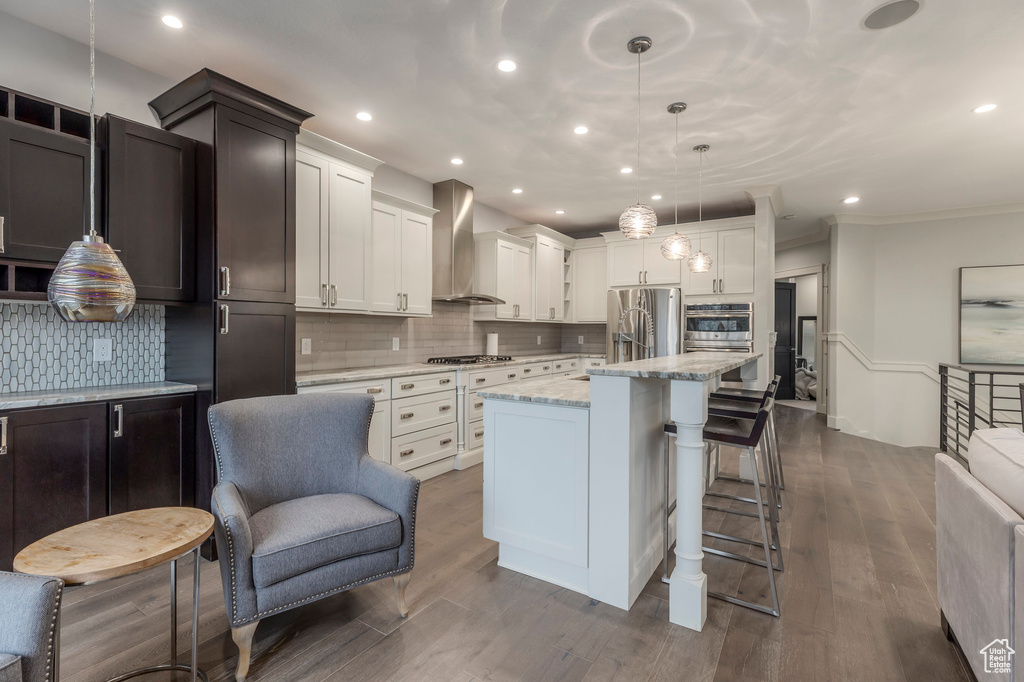 Kitchen with a kitchen breakfast bar, a center island, recessed lighting, wall chimney exhaust hood, and stainless steel appliances