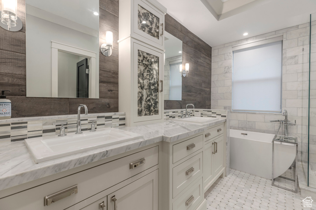 Full bathroom with double vanity, a sink, a freestanding bath, and tile walls