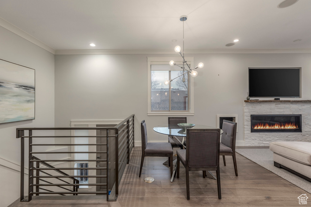 Dining area with a fireplace, wood finished floors, baseboards, an inviting chandelier, and ornamental molding