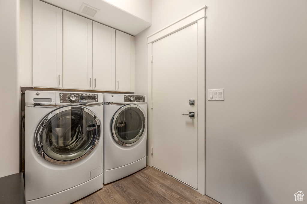 Clothes washing area with cabinet space, washer and clothes dryer, and wood finished floors