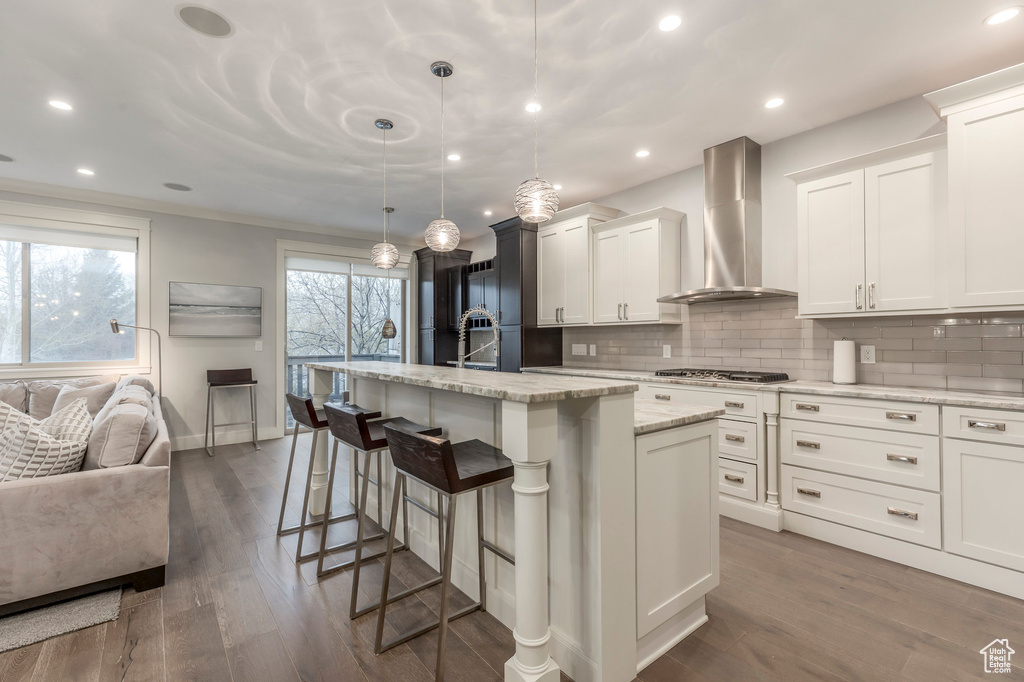 Kitchen featuring wall chimney range hood, dark wood-style flooring, a kitchen island with sink, and tasteful backsplash