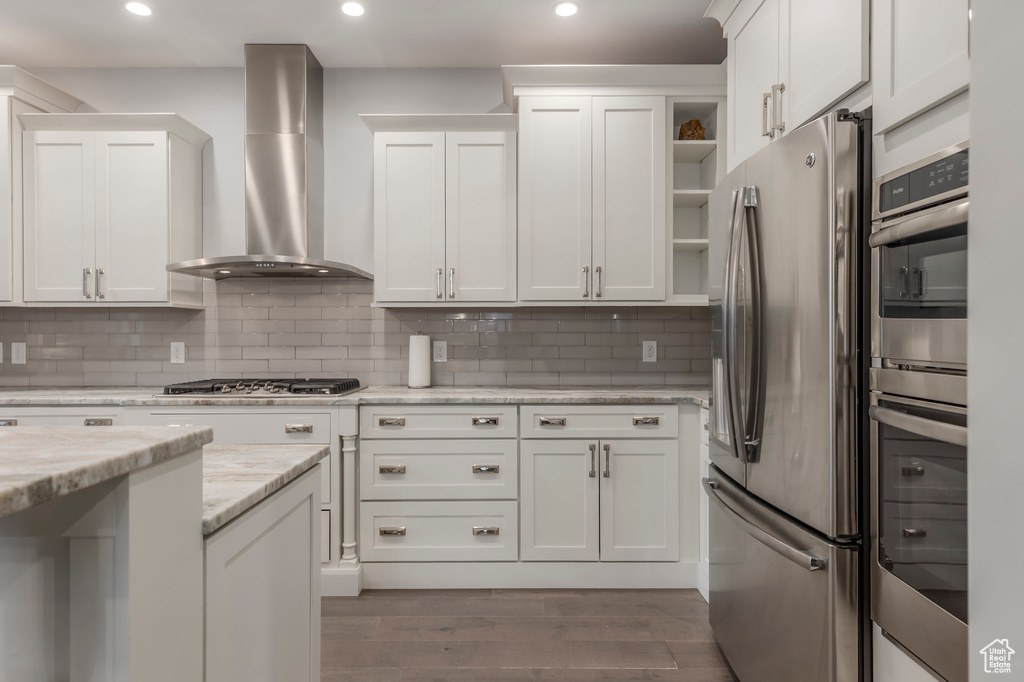 Kitchen with appliances with stainless steel finishes, open shelves, white cabinetry, wall chimney exhaust hood, and dark wood-type flooring