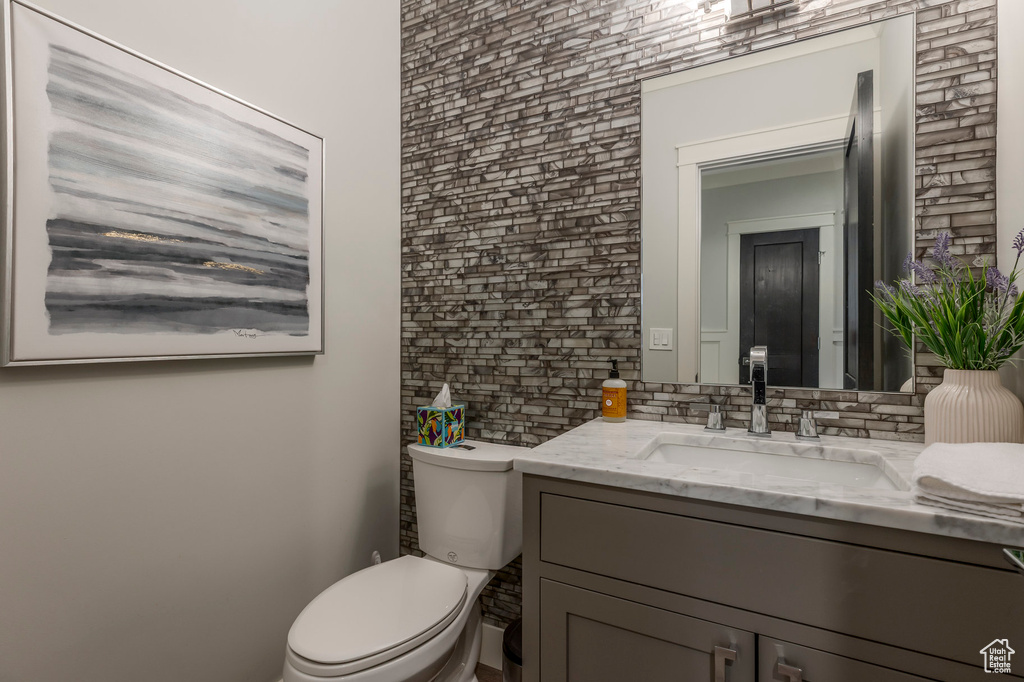 Bathroom featuring vanity, brick wall, and toilet