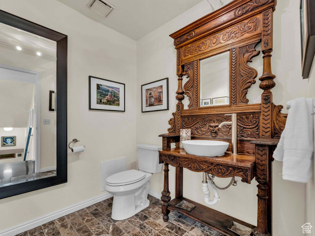 Bathroom featuring a sink, toilet, baseboards, stone finish flooring, and visible vents