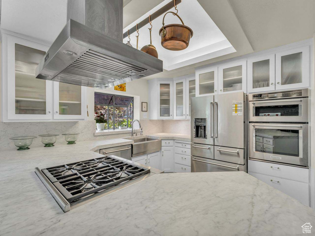 Kitchen featuring island range hood, white cabinetry, light stone counters, a sink, and stainless steel appliances