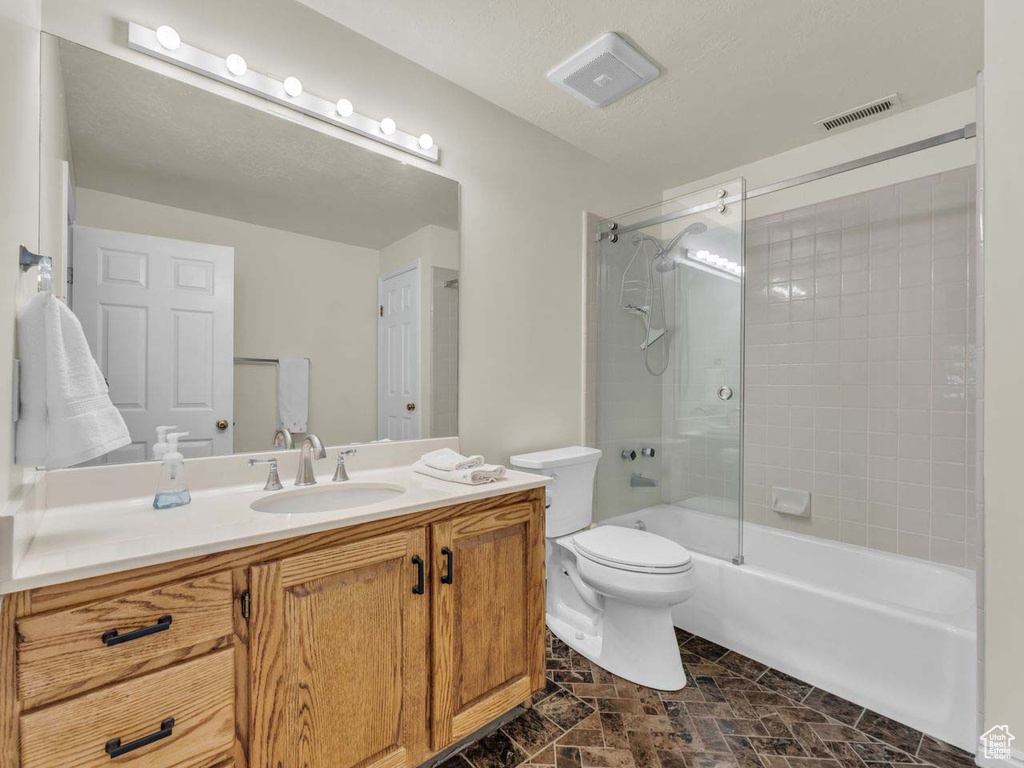 Full bath featuring bathtub / shower combination, vanity, toilet, stone finish floor, and visible vents