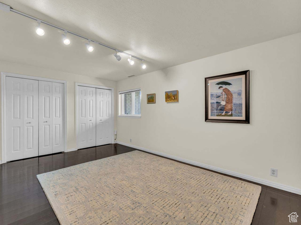 Unfurnished bedroom featuring baseboards, two closets, rail lighting, and dark wood-type flooring