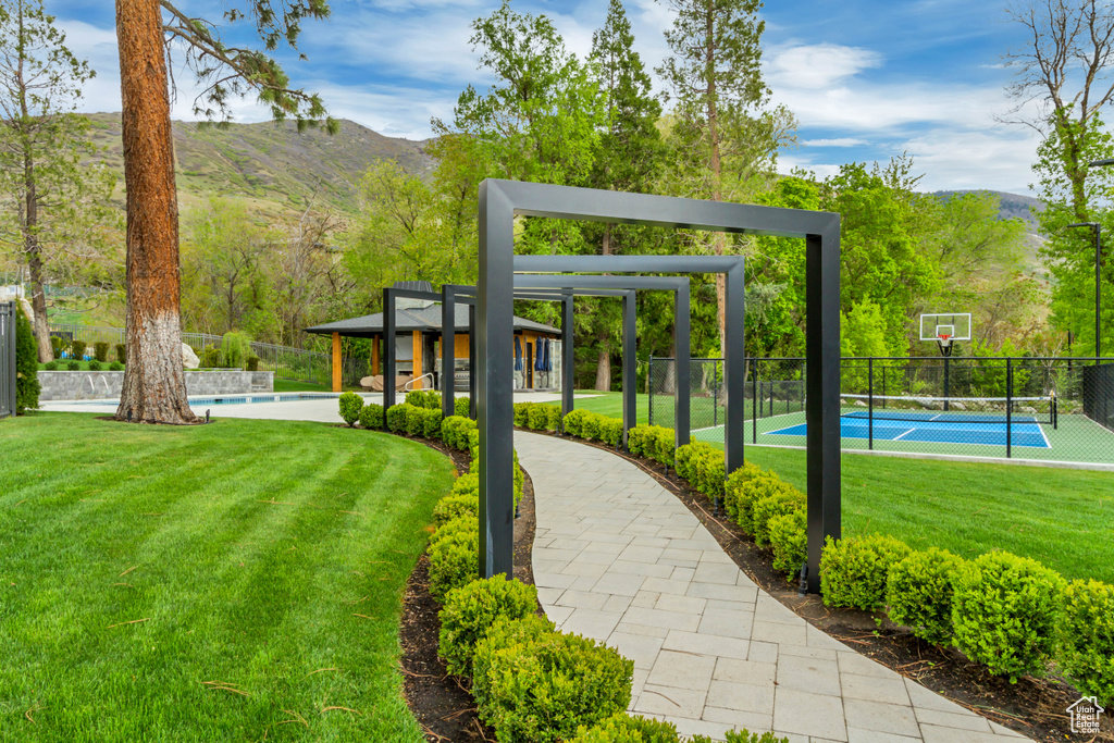 View of property\'s community with a lawn, a tennis court, fence, and a mountain view