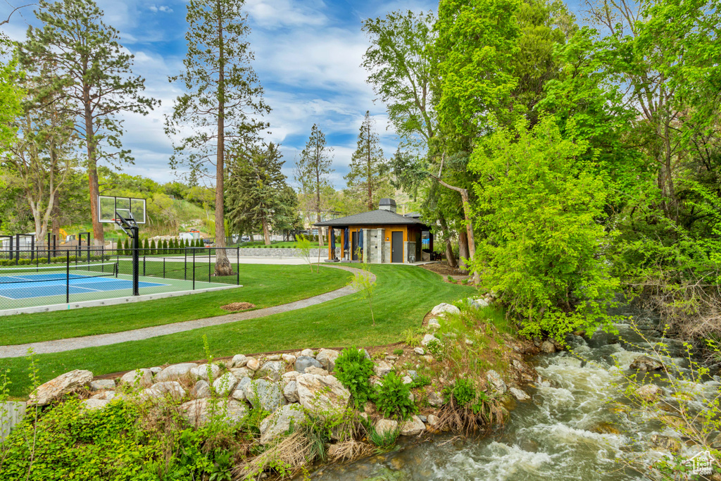 View of property\'s community featuring a yard, a tennis court, fence, and community basketball court