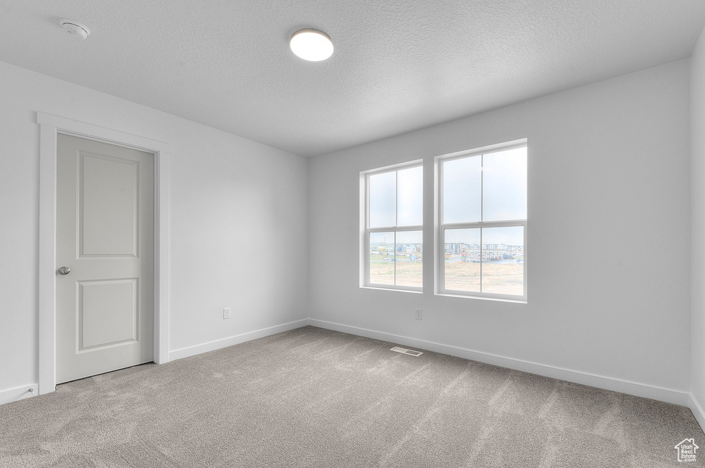 Carpeted spare room with baseboards, a textured ceiling, and visible vents