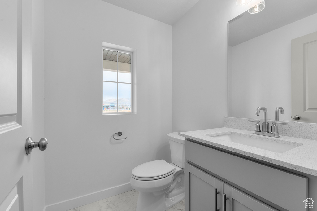 Half bath featuring toilet, baseboards, marble finish floor, and vanity