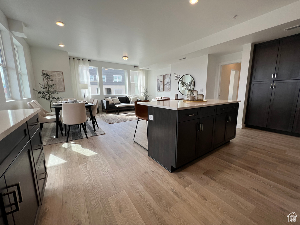 Kitchen featuring visible vents, a center island, light countertops, dark cabinetry, and light wood-style flooring