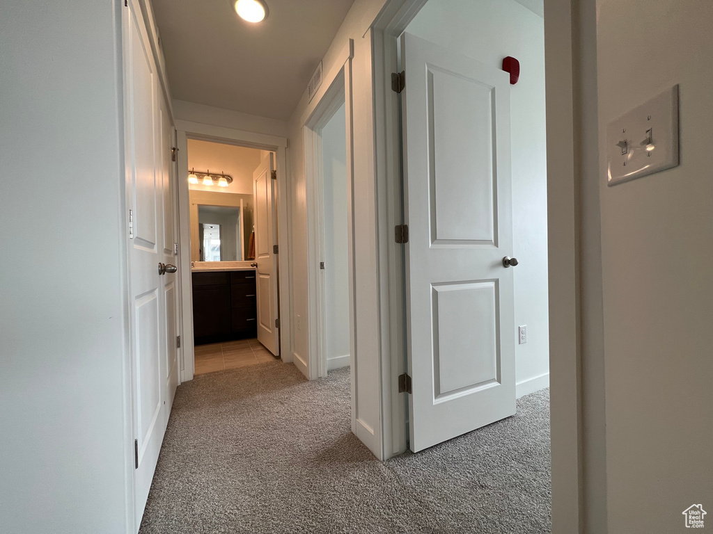Hallway with visible vents, baseboards, and light carpet