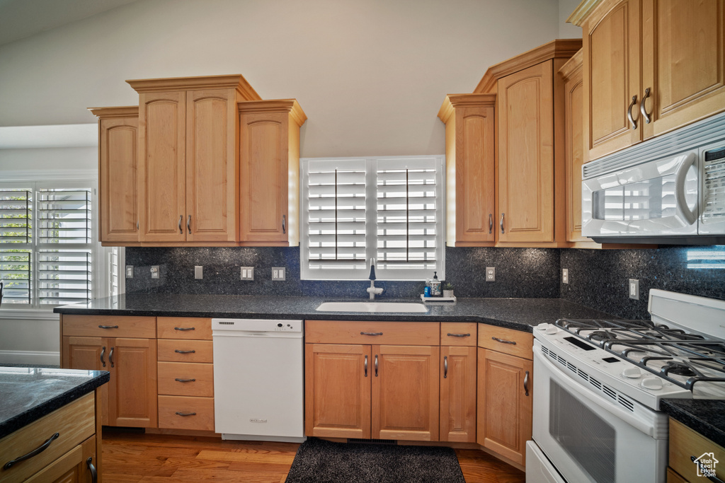 Kitchen with wood finished floors, white appliances, a sink, and light brown cabinetry