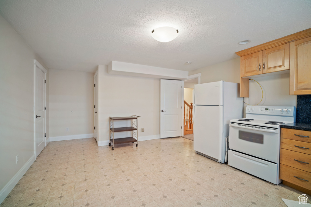 Kitchen featuring dark countertops, white appliances, baseboards, tasteful backsplash, and a textured ceiling