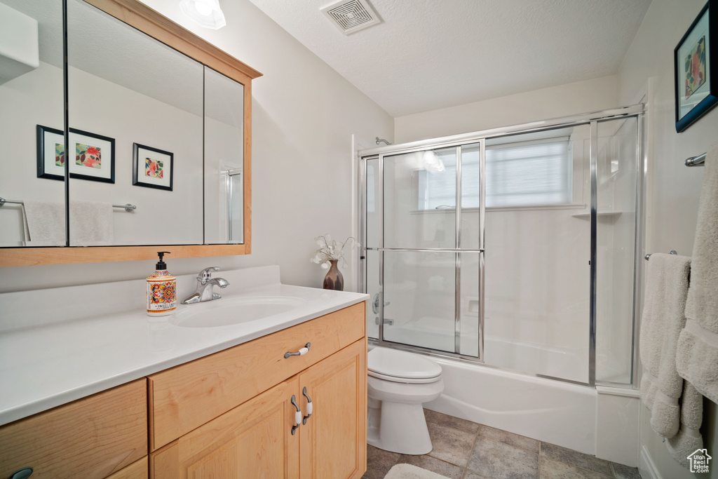 Full bathroom featuring enclosed tub / shower combo, stone finish floor, visible vents, toilet, and vanity